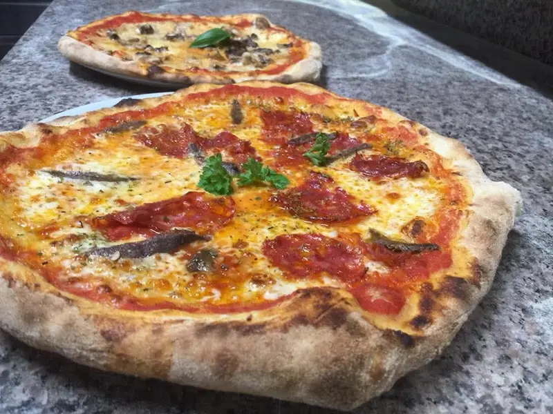 Frisch gebackene Steinofenpizza mit Salami, Sardellen und Basilikum